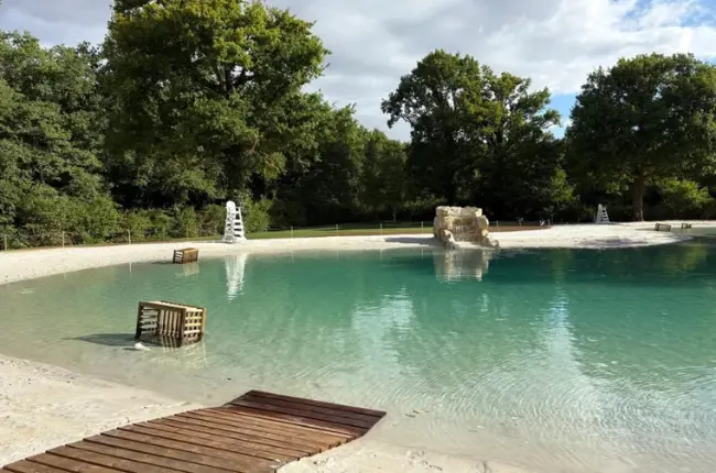 A communal lagoon with turquoise water and a beach area set in natural landscaping for shared use