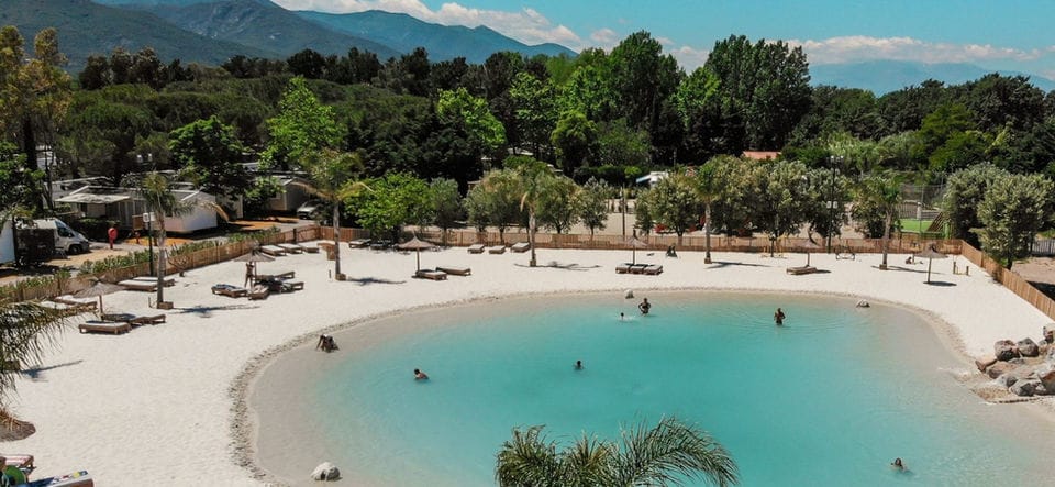 A lagoon with turquoise water and a white beach set in a mountain valley, forest and distant ridges behind