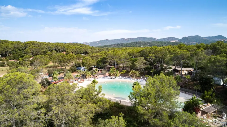 Aerial view of a lagoon with a curved white-sand cove, turquoise water, surrounded by green forest with mountains beyond